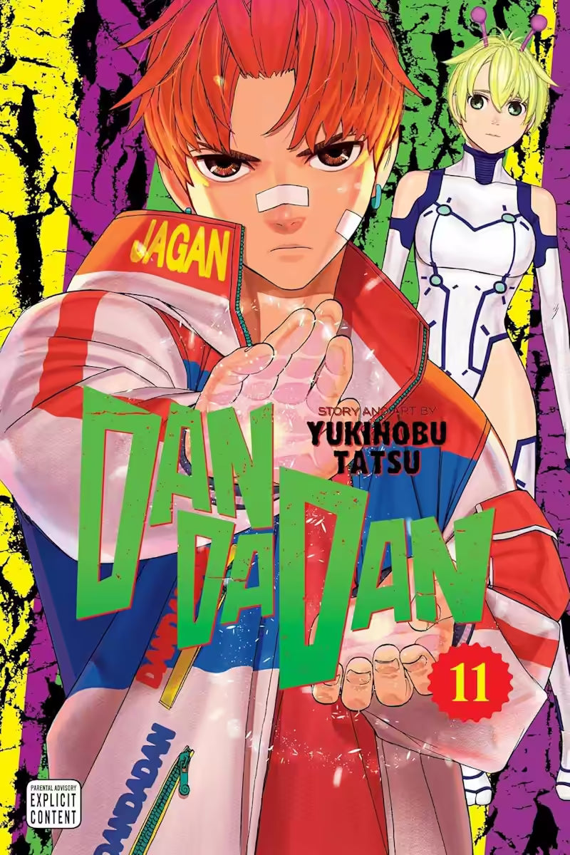 Manga forside til ‘Dandadan’ bind 11, der viser en rødhåret ung mand i træningsjakke med hånden fremstrakt, mens en ung kvinde med antenner står bag ham mod en farverig, revnet baggrund.