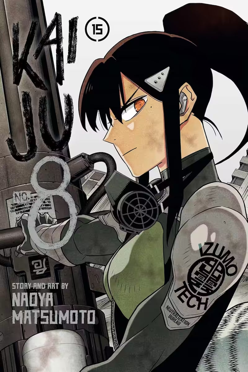 Manga forside til ‘Kaiju No. 8’ bind 15, der viser Mina Ashiro i profil, iført taktisk udstyr og med et stort kanonvåben bag sig, sat mod en lys, grålig baggrund.